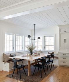 a dining room table with four chairs and a bench in front of two windows that are open