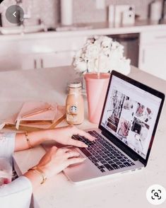 a woman is typing on her laptop at the kitchen counter with flowers in vases