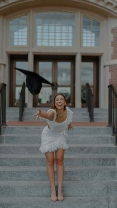 a woman in a white dress is standing on some steps and throwing a graduation cap into the air