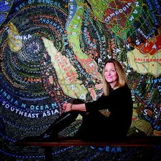 a woman sitting on a bench in front of a wall with words all over it