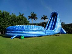 an inflatable water slide is on the grass with palm trees and blue sky