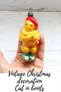 a hand holding a yellow bear ornament with the words vintage christmas decoration cat in boots