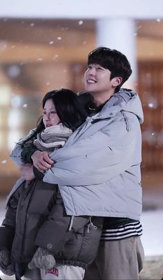 a man and woman are hugging in the snow while wearing winter coats on their shoulders