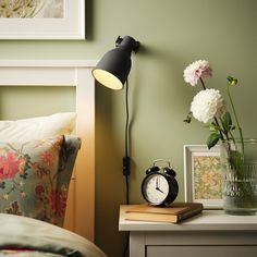 an alarm clock sitting on top of a table next to a lamp and vase with flowers