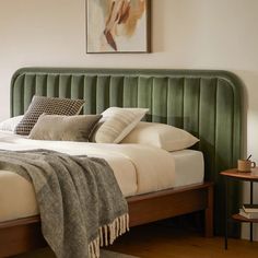 a bed with green headboard and pillows on top of it next to a table