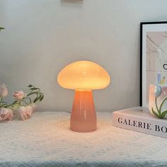 a mushroom shaped lamp sitting on top of a table next to a book and flowers