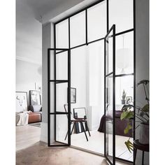 an open glass wall in a room with white walls and wood floors, along with plants