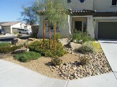 a house with rocks and plants in front of it on the side of the road