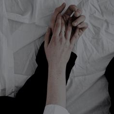 two hands touching each other on top of a white sheet covered bed in the dark