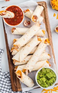 burritos with salsa and guacamole on a wooden platter next to condiments