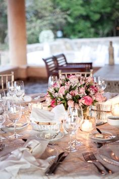 the table is set with silverware and pink flowers in vases, candles and napkins