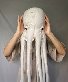 a woman covering her face with an octopus mask in front of her head and hands