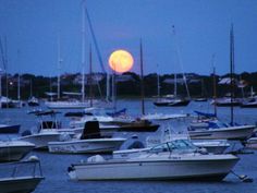 the full moon is setting over boats in the water