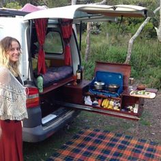 a woman standing in front of an open van with food and drinks on the back