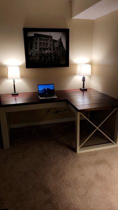 a laptop computer sitting on top of a wooden desk next to two lamps and a painting