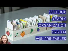 a woman standing in front of a wooden box filled with cards and folders that are labeled seedbox yearly organization system with printables