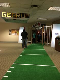 a man walking down a green carpeted hallway next to a sign that says game time