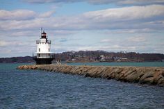 a light house sitting on top of a rock wall next to the ocean with clouds in the sky