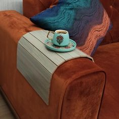 a coffee cup sitting on top of a wooden table next to a brown couch with blue pillows