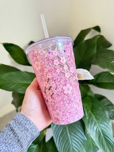 a person holding up a pink cup with flowers on it and a straw in their hand