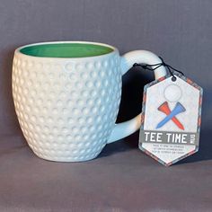 a white coffee mug with a green rim and tag hanging from it's side