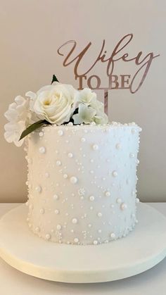 a wedding cake with white flowers and a sign that says wife to be on it