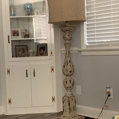 a lamp sitting on top of a wooden floor next to a white cabinet and window