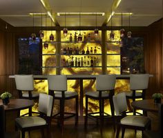 a dimly lit bar with stools and bottles on the wall behind it in front of a large window