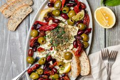 a platter filled with olives, bread and other food on a wooden table