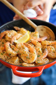 a red pan filled with cooked shrimp and lemon wedges