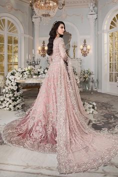 a woman in a pink gown standing next to a chandelier and flower arrangement