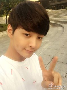 a young man giving the peace sign in front of an empty area with steps and trees