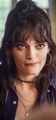 a close up of a person with long hair and piercings on her nose, looking at the camera