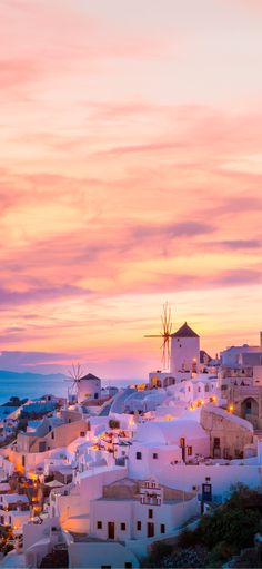 the sun is setting over white buildings and windmills in oiai, greece