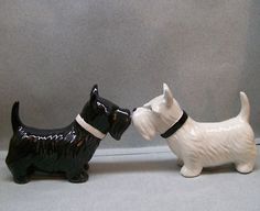 two black and white ceramic dogs facing each other on a gray surface with grey wall in the background