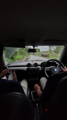 two people sitting in the driver's seat of a car driving down a road