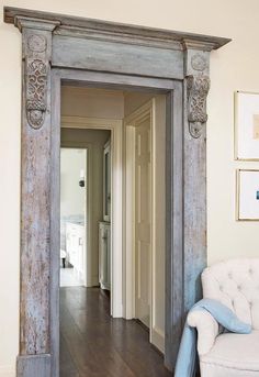 an open door leading into a living room with a white chair and pictures on the wall