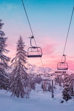 a ski lift with two people on it in the middle of snow covered trees at sunset