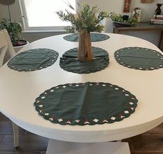 a white table topped with green placemats next to a vase filled with flowers