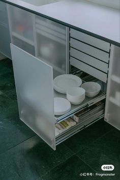 an open cabinet with plates in it on the floor and drawers below them that are empty