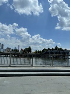 a bench sitting on the side of a road next to a river under a cloudy blue sky