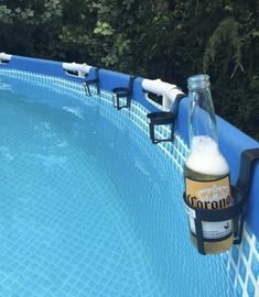 a beer bottle sitting on top of a blue swimming pool next to a green forest