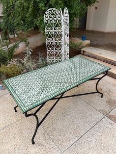 a green and white table sitting on top of a stone floor next to some bushes