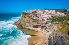 an aerial view of a beach with houses on the cliff and ocean in the foreground