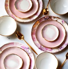 pink and white plates with gold rims are arranged on a marble table top, next to golden spoons