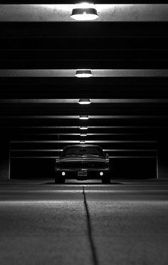 a black and white photo of a car parked in a parking garage with lights on