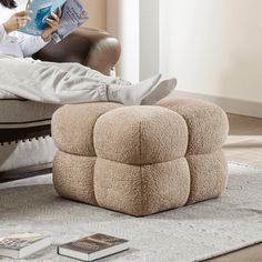 a woman sitting in a chair reading a book with her feet up on the ottoman