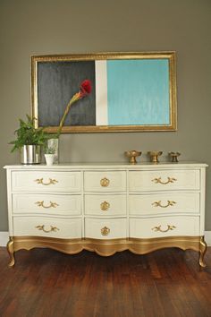 a white and gold dresser with a red rose on it in front of a painting