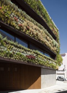 a building with plants growing on it's side and two cars parked in front