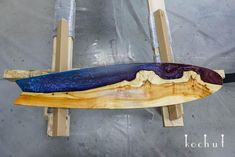 a wooden surfboard sitting on top of a piece of plywood with blue and purple paint